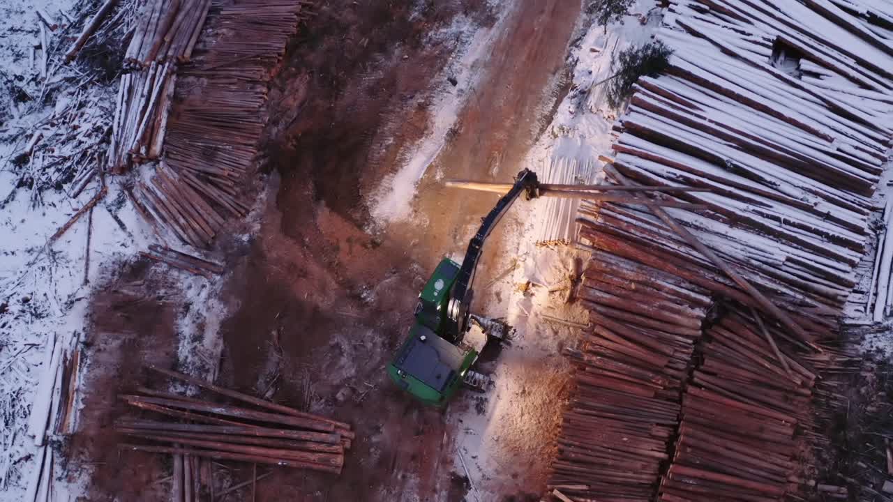dramático de arriba hacia abajo primer plano toma aérea de manipulador de madera cargando transporte de madera camión de 18 ruedas desde montones cubiertos de nieve cercanos de pinos maduros cortados