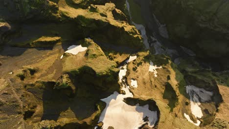 drone shot of an icelandic canyon with patches of snow, rugged cliffs, and sunlight casting dramatic shadows across the terrain