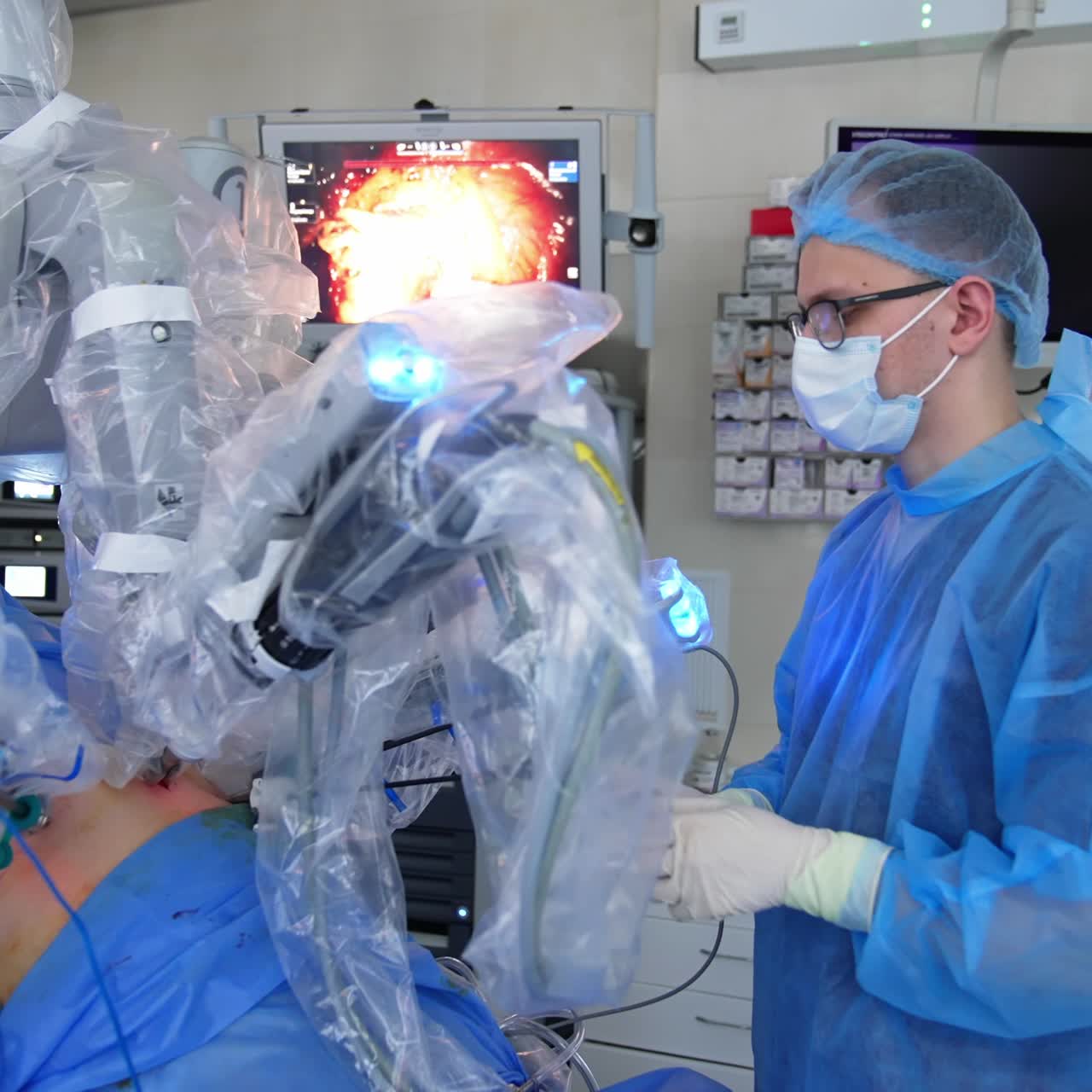 Young adult male surgeon stand still holding instrument input into patient's body and looking at the screen. Da Vinci robot doing the microsurgery