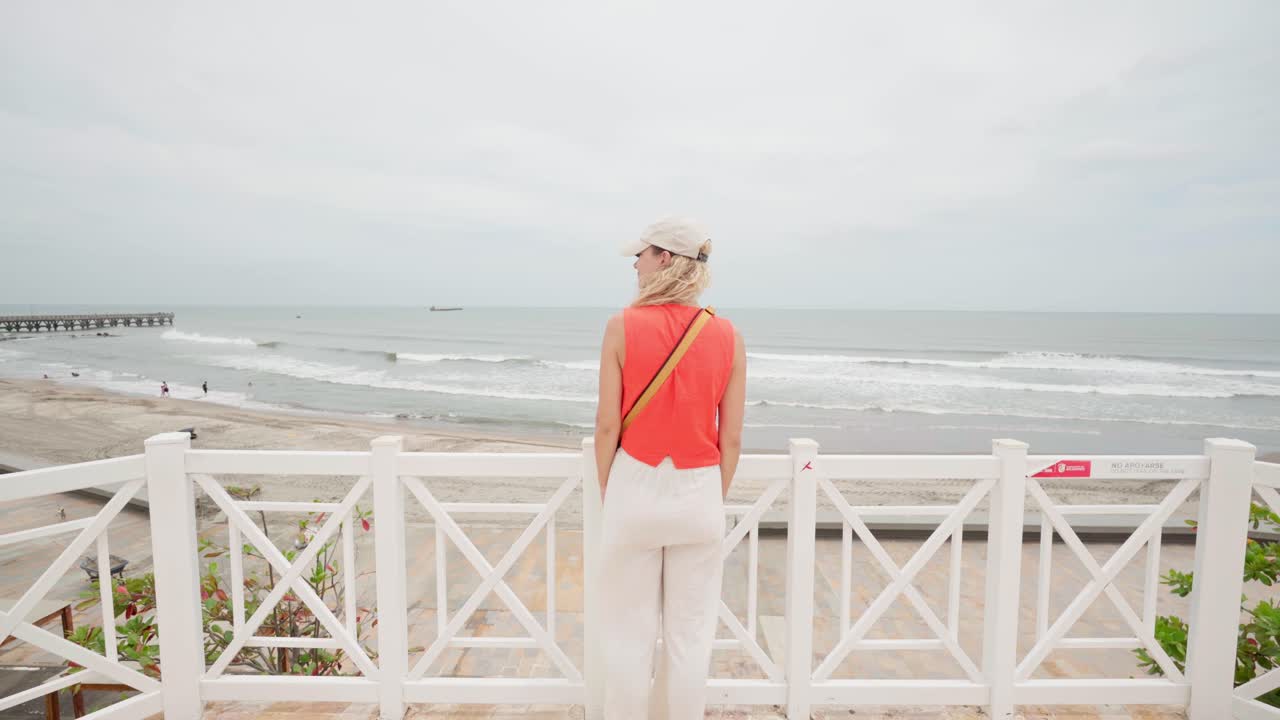 Rear view of a blonde woman enjoying the scenic ocean view from a white wooden pier, puerto colombia