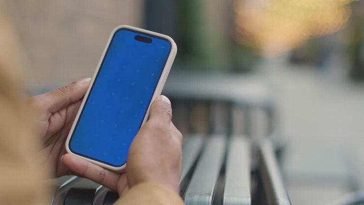 Primo piano di un uomo musulmano seduto all'aperto in una strada della città mentre guarda un telefono cellulare con schermo blu