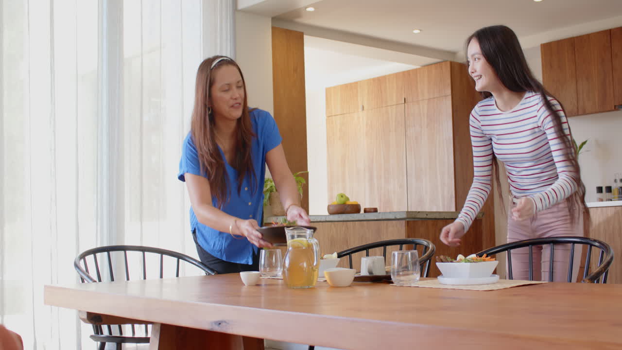 Setting table, asian mother and daughter preparing meal together in modern kitchen