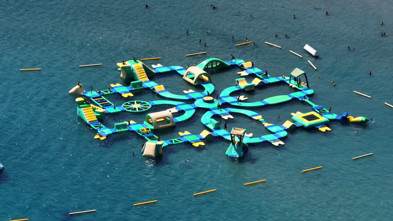 Aerial view orbiting a inflatable water adventure park at the sea, summer day
