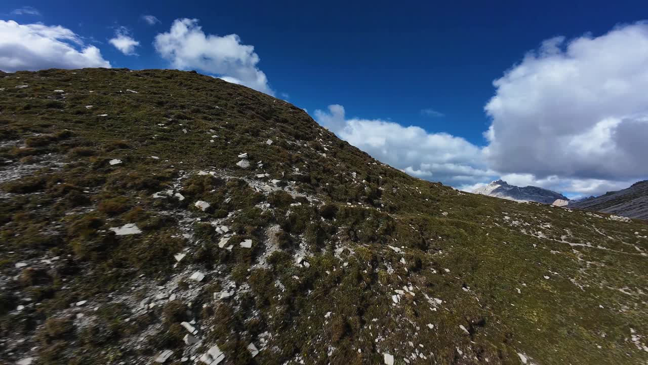 FPV drone video featuring a dynamic flight over the grass fields and mountain tops of the Dolomites, Italian Alps. FPV cinematography, iconic landscape, and natural setting
