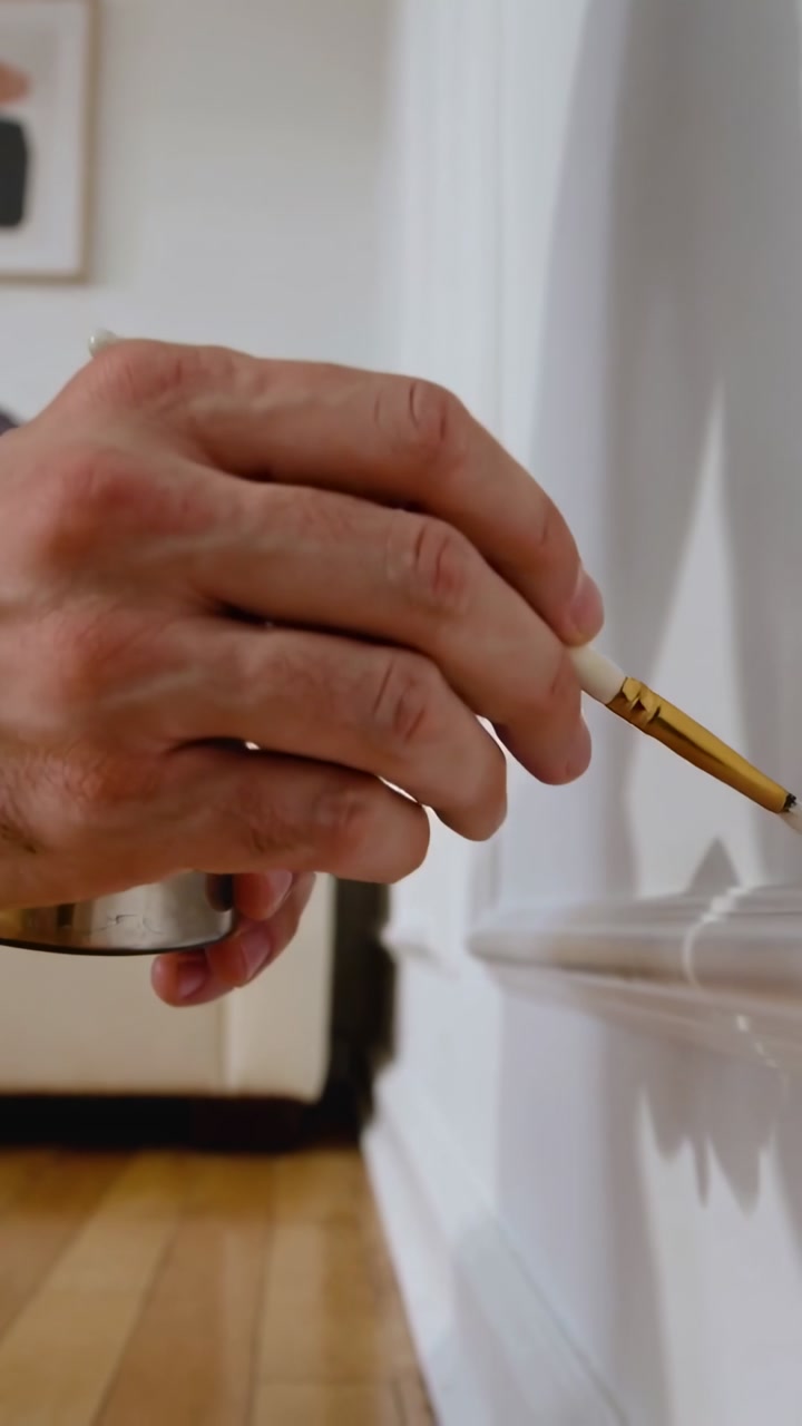 Vertical video: Starting touchup, male hand wearing shirt painting trim in home, using small brush