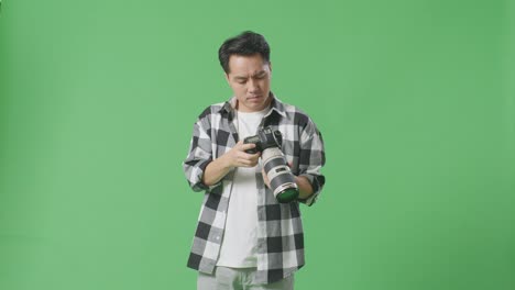 asian photographer taking pictures then looking at them in the camera being unsatisfied with his work while standing on green screen background in the studio