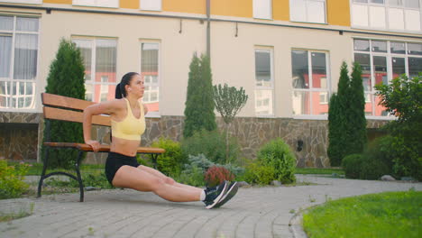 Una-Mujer-Se-Levanta-En-Un-Banco-Del-Parque-Contra-El-Fondo-De-Los-Edificios-En-Cámara-Lenta.-Entrenamiento-En-El-Parque-De-La-Ciudad