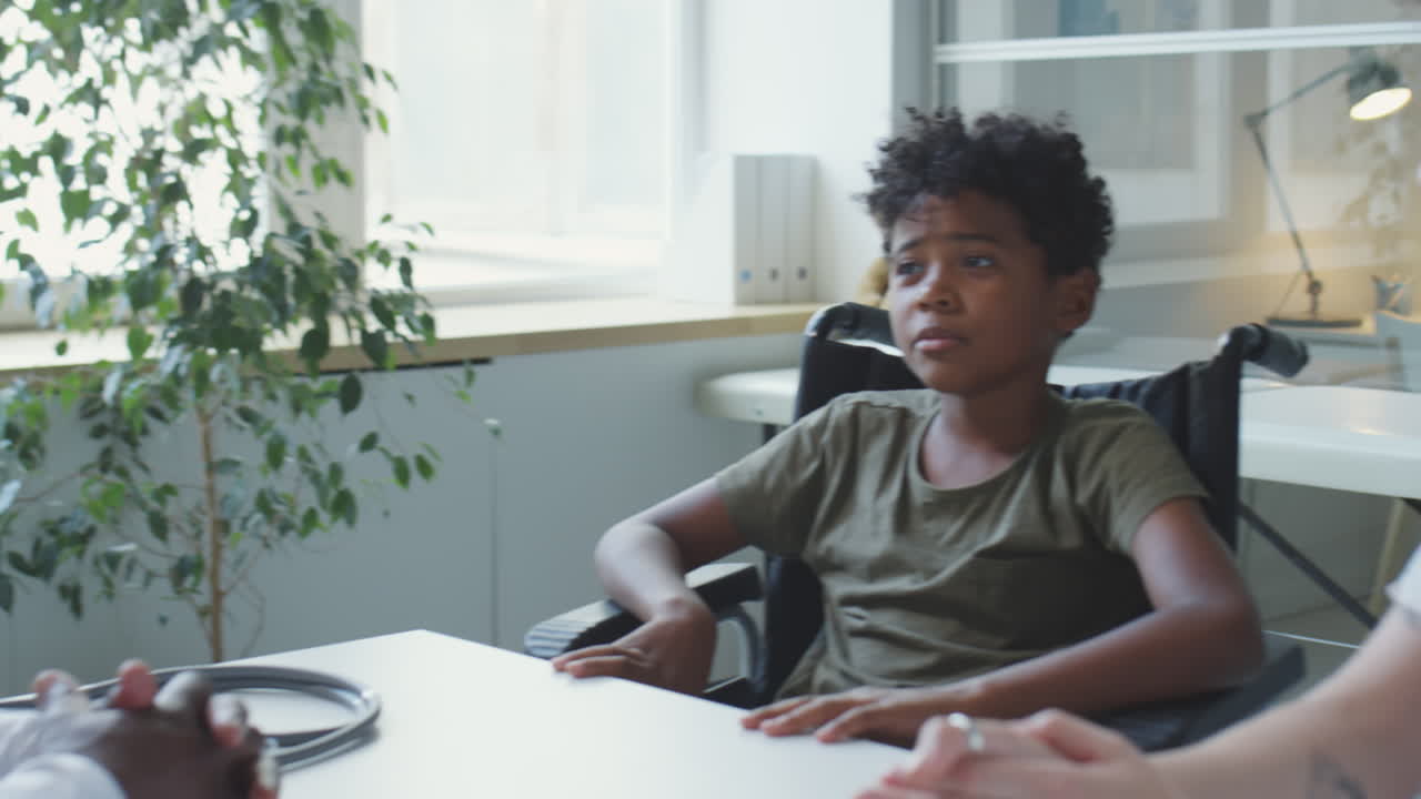 A young boy in a wheelchair is talking to a woman in an office