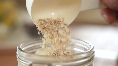 hand pouring oat flakes in glass jar, slow motion, extreme close up view