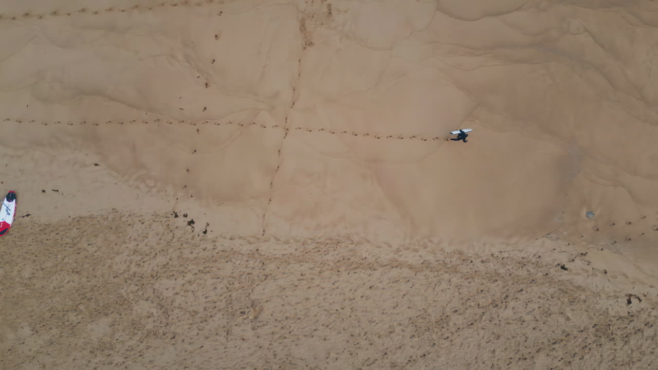 Surfboarder walking golden sand leaving footprints top view. Unknown surfer