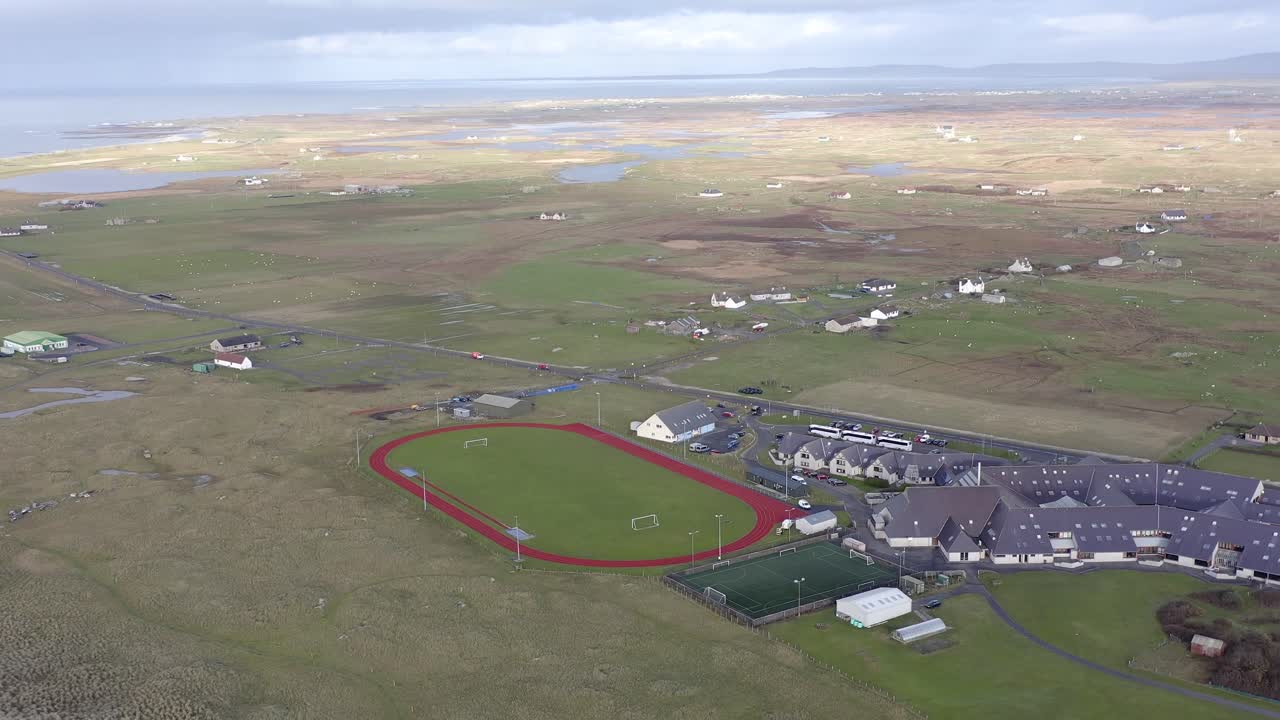 uhi 대학 캠퍼스와 benbecula 섬의 어두운 섬 호텔을 향해 트랙과 피치를 가로지르는 넓은 각도 드론  ⁇