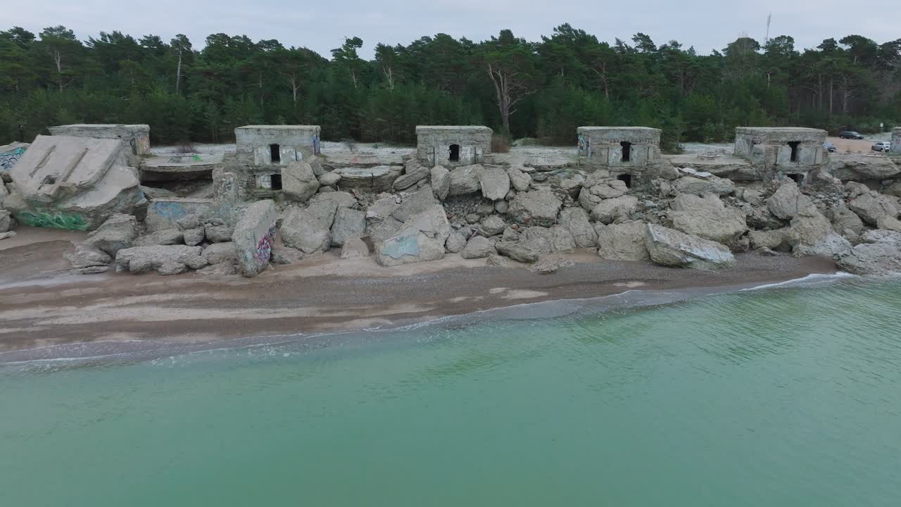 vista aérea de los edificios de fortificación costeros abandonados en los fuertes del norte de karosta en la playa del mar báltico, olas salpicadas, día nublado, amplio y revelador disparo de drones moviéndose hacia atrás