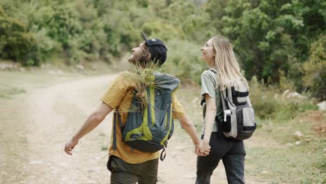 a happy couple backpackers walking by forest's path and holding hands