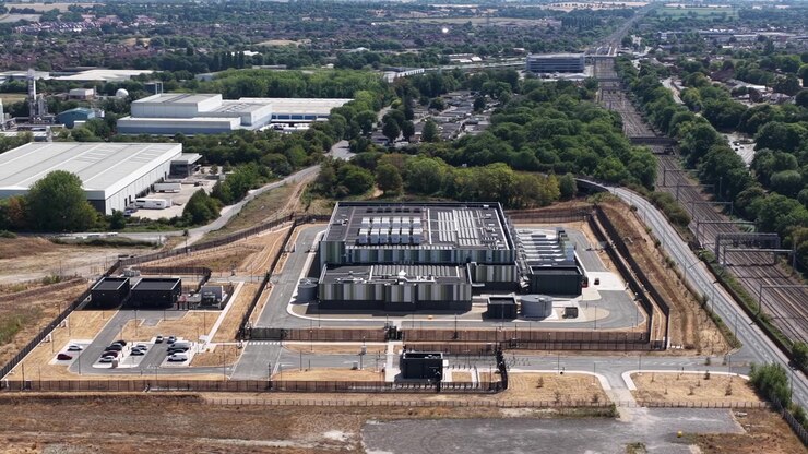 High angle drone view of a massive data center facility featuring HVAC cooling units, power substations, and modern architecture powering cloud networks and AI systems.