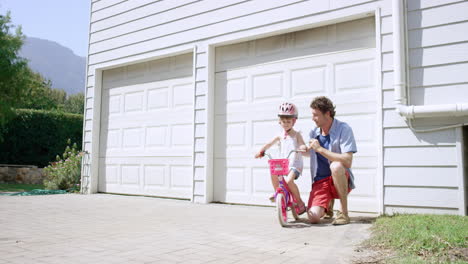 father teaching daughter how to ride a bicycle