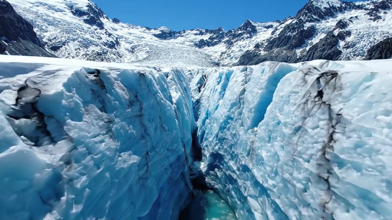 Majestätische Gletscherlandschaft: Eine Luftaufnahme von Rissen und Spalten in einem atemberaubenden Eisfeld unter klarem blauem Himmel.