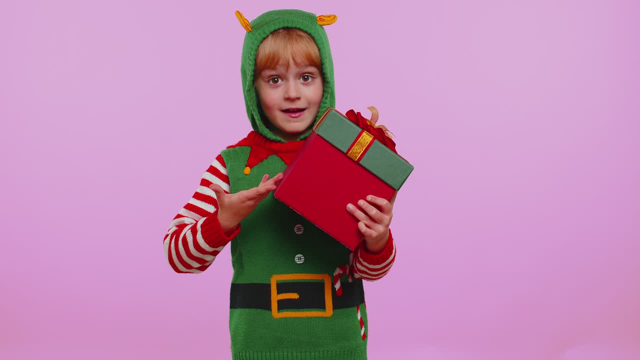 Zábavná dospívající batolecí holčička v kostýmu vánočního Santy představuje vánoční dárkovou krabici s nákupní akcí