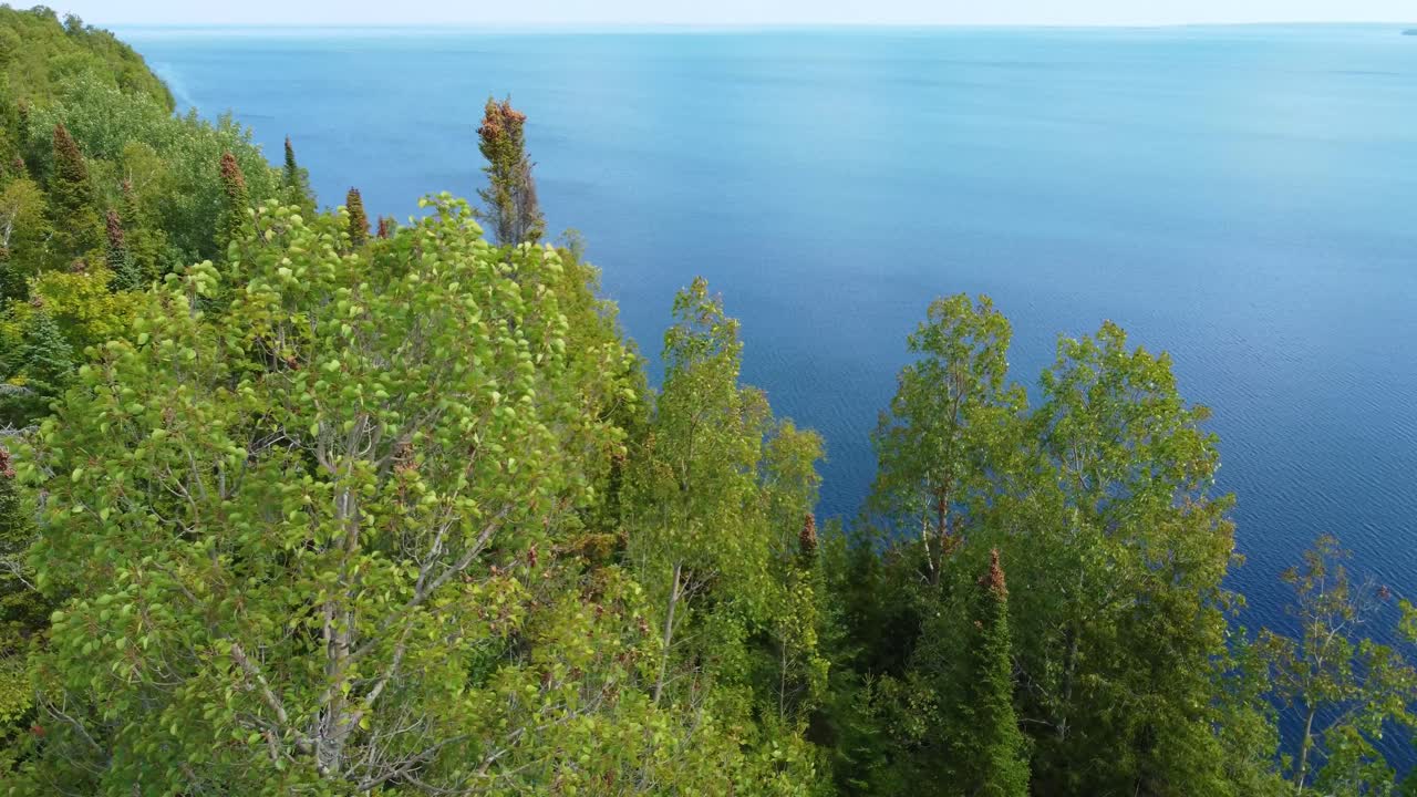 Luftaufnahme eines blauen Sees mit Steinufer und grünem Wald.