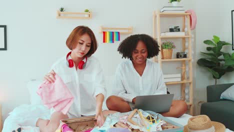 una pareja de lesbianas multiétnicas empacando una maleta para viajar.
