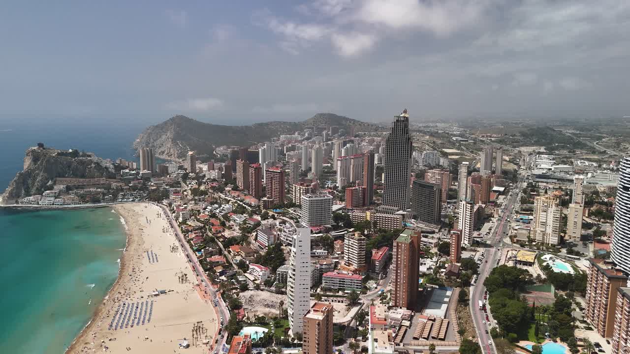 Benidorm's famed coastline, Spain: A high, forward drone flight offers a sweeping aerial of the beach, backed by its dense, modern skyscraper skyline on the Mediterranean.