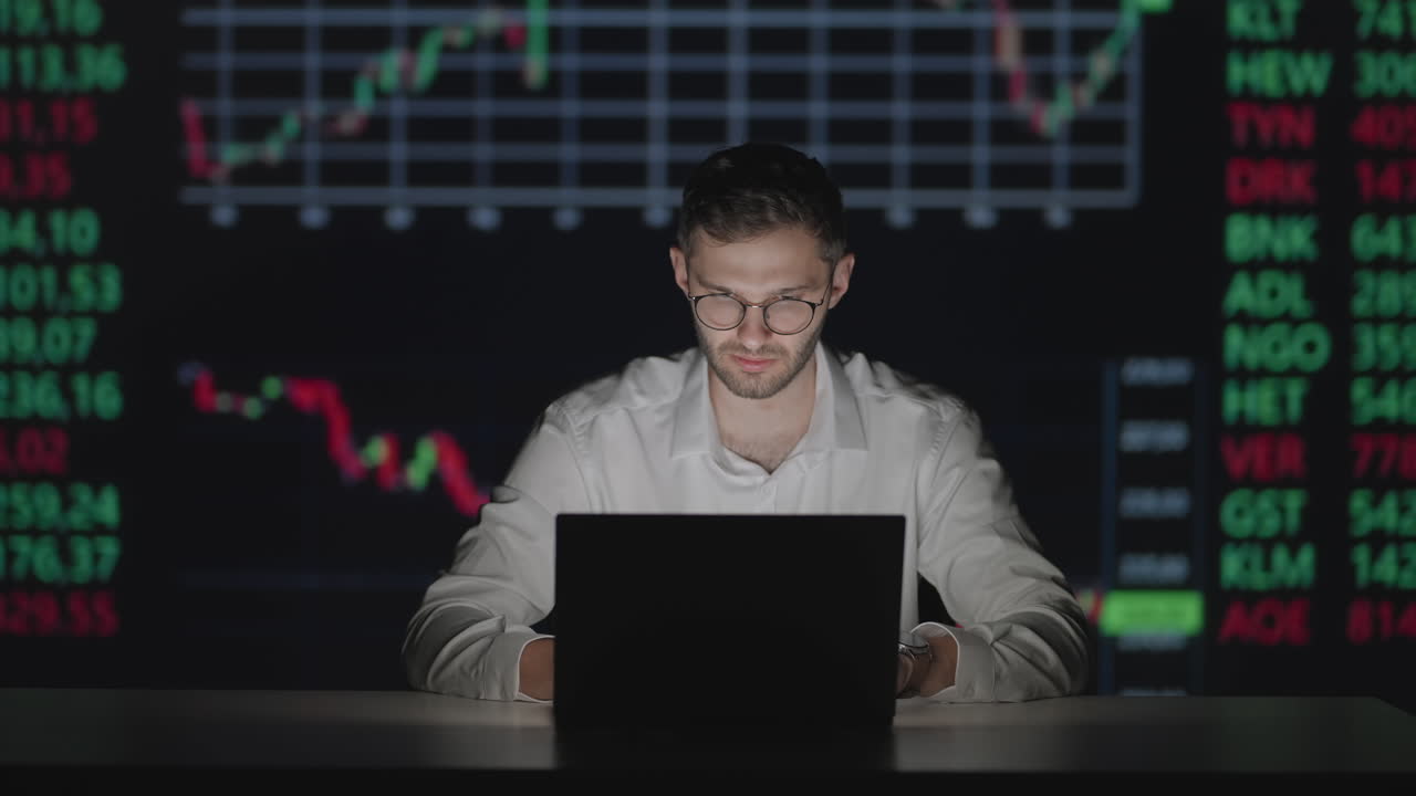 Young Caucasian man trader working at monitor laptop and browsing online in trading office. Male broker following rates and bets. Manager texting at screen.