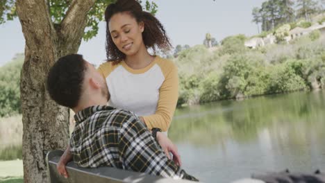 happy african american couple sitting on bench at lake in forest, slow motion