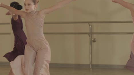 a group of young ballet students in black dancewear practicing positions in a spacious ballet studio with wooden flooring and wall-mounted barres. focused expressions and synchronized movements.