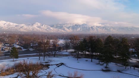 seagulls soar above snow covered icy pond in park with epic view of wasatch mountains and downtown salt lake in winter