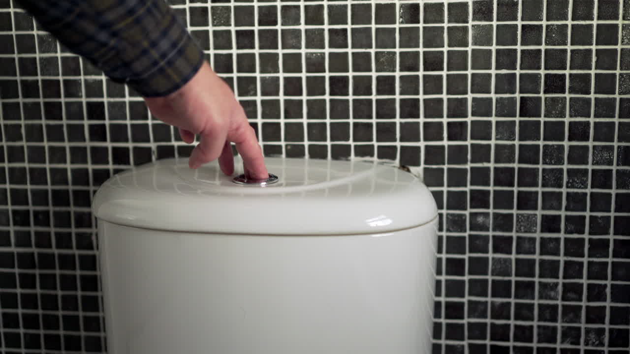 변기 물을 내리는 남자의 손, 흰색 수조 크롬 버튼을 눌렀습니다.