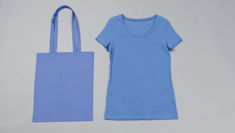 Close-up-of-blue-bag-and-t-shirt-on-grey-background,-with-copy-space,-slow-motion