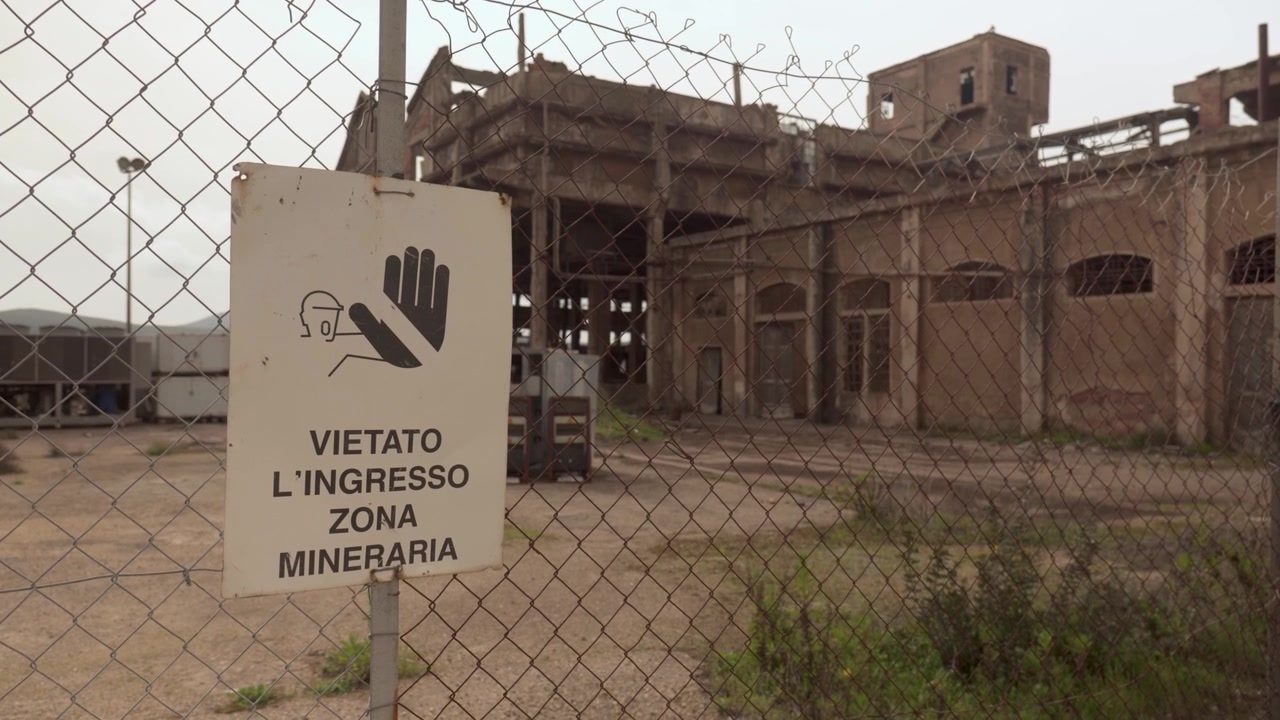 No Entrance-Mining Area Sign On The Fence With Abandoned Building In The Historic Monteponi Mining Site In Iglesias, Sardinia, Italy. Static Shot
