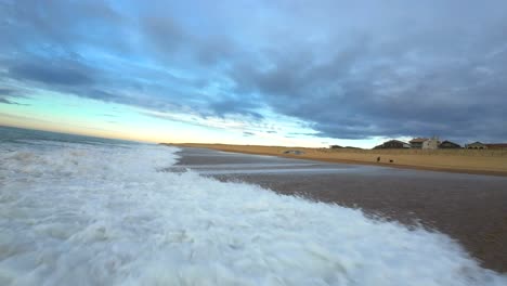 Vuelo-Fpv-De-Baja-Altitud-Sobre-Las-Olas-En-La-Playa-De-Surf-De-Hossegor-Durante-Una-Puesta-De-Sol-Nublada