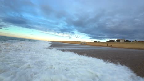 vuelo fpv de baja altitud sobre las olas en la playa de surf de hossegor durante una puesta de sol nublada