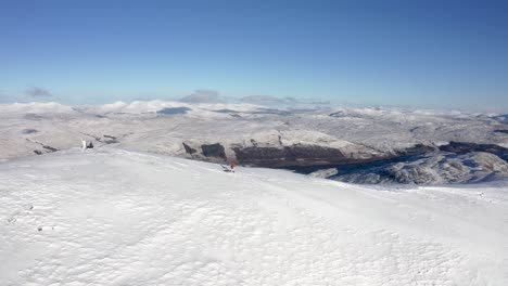 Person-walking-dog-in-snow-capped-summit-under-blue-sky