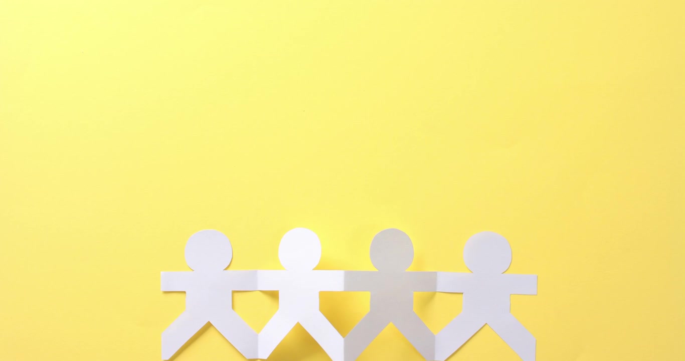 Close up of people holding hands made of white paper on yellow background with copy space