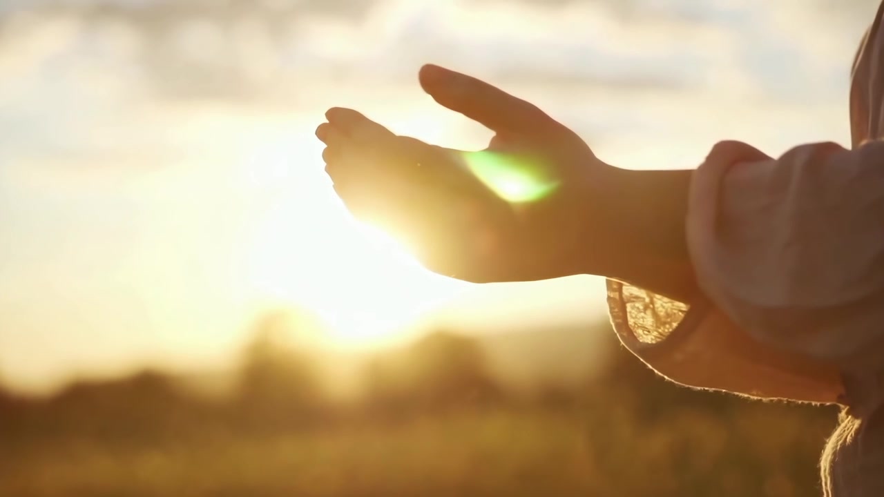 Mani a coppa che si protendono verso la luce dorata del sole al tramonto