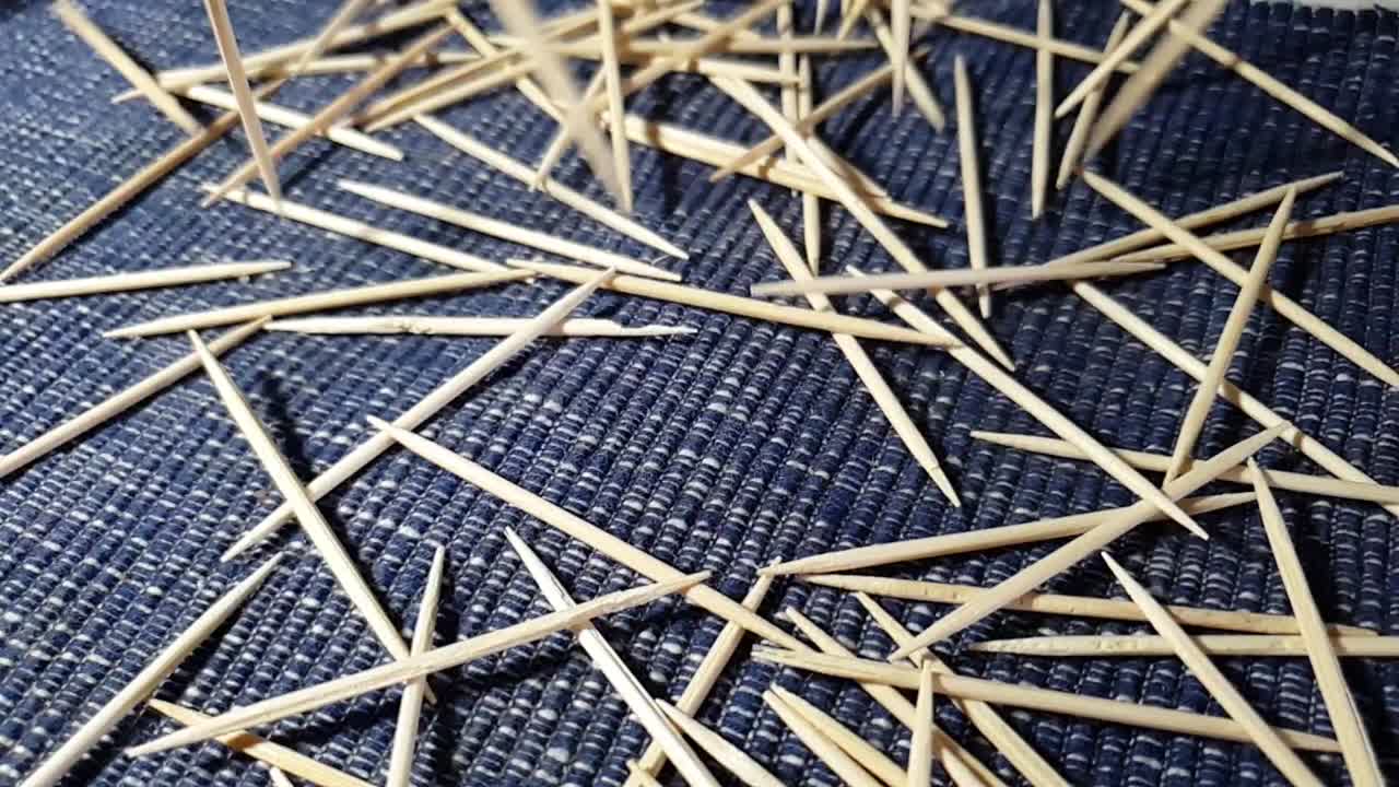 manojo de palillos de madera que caen a cámara lenta sobre el mantel rodando y aterrizando al azar