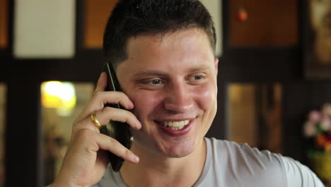 a steady handheld close-up shot of a young white man, in his 30s , talking on the phone and smiling, the man is wearing a wedding ring