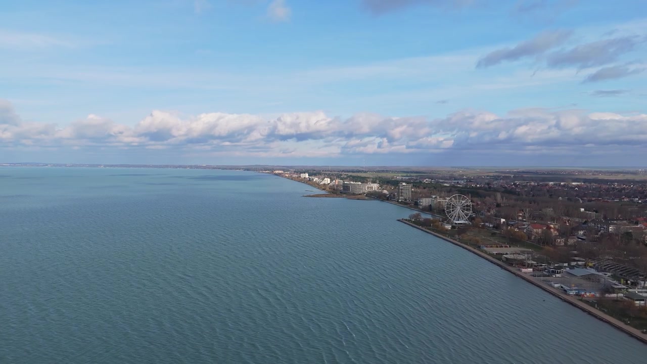 A Siófok, sul Lago Balaton, una vista drone cattura il lungomare urbano con la sua passeggiata, la spiaggia, gli edifici moderni, il verde e una prominente ruota panoramica in una nuvolosa giornata invernale