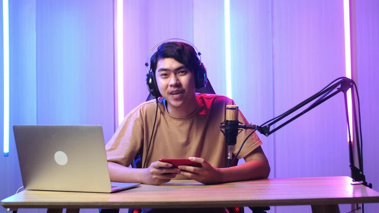 Uomo asiatico che tiene in mano un telefono cellulare e parla alla telecamera durante una diretta streaming.