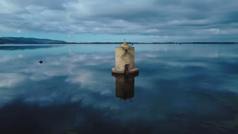 Old-Spanish-windmill-in-the-lagoon-at-the-island-town-Orbetello-close-to-Monte-Argentario-and-the-Maremma-Nature-Park-in-Tuscany,-Italy,-with-blue-sky-and-calm-blue-water