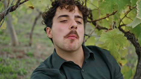 retrato joven viticultor sentado bajo la vid comiendo uvas. trabajador relajándose.