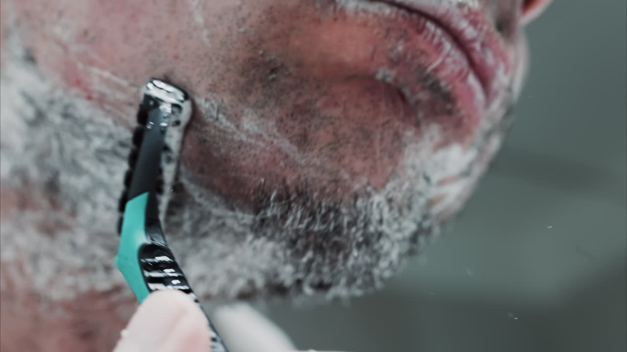 Close up of a man shaving his beard with a razor