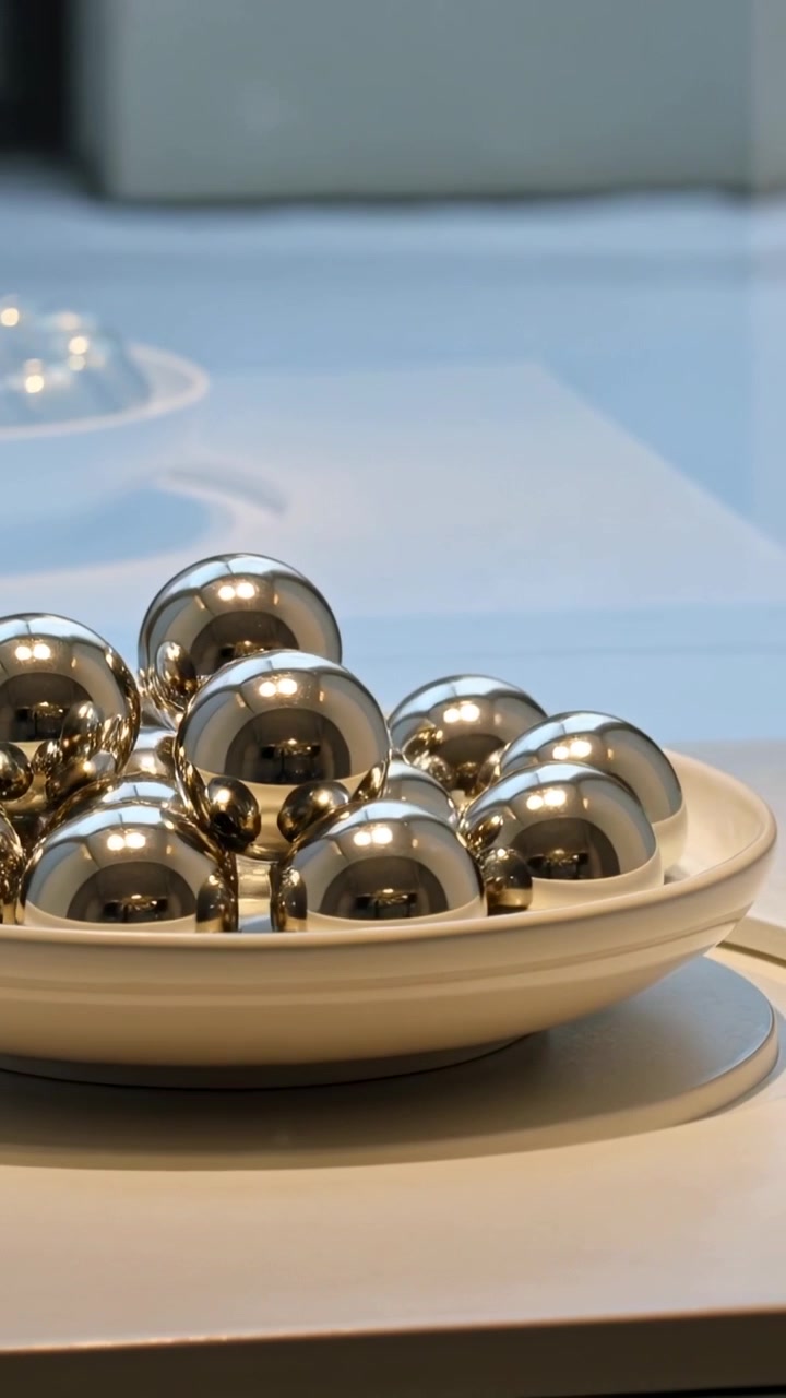 Vertical video: Moving camera revealing steel balls shifting glints and center on table, white dish