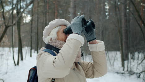 senior woman with binoculars in a snowy forest