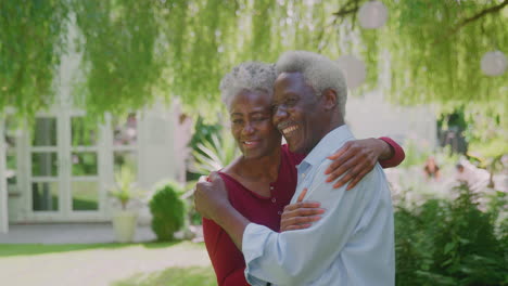 Loving-Senior-Couple-Standing-In-Garden-At-Home-And-Hugging-After-Retirement