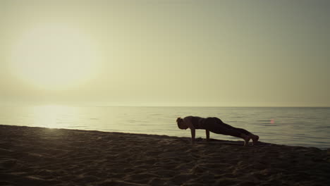 silhouette sportswoman making plank pose practicing yoga. girl training on beach