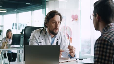 close-up view of caucasian male doctor sitting at desk with laptop and explaining to male patient treatment for coronavirus in medical consultation