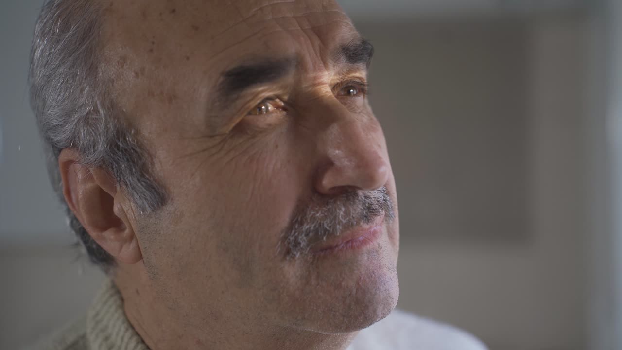 un anciano pensativo mirando por la ventana.