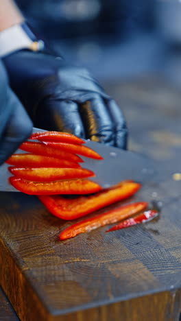 chef wearing black gloves cut the red pepper into slices. preparing dishes of fresh vegetables. close up. blurred backdrop. vertical video.